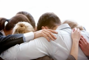 Circle of business people embracing each other with their heads bowed while concentrating